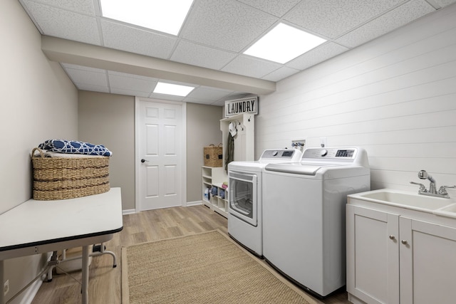 laundry area featuring separate washer and dryer, sink, wooden walls, and light wood-type flooring