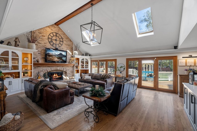 living room featuring a notable chandelier, wood-type flooring, lofted ceiling with beams, a brick fireplace, and french doors