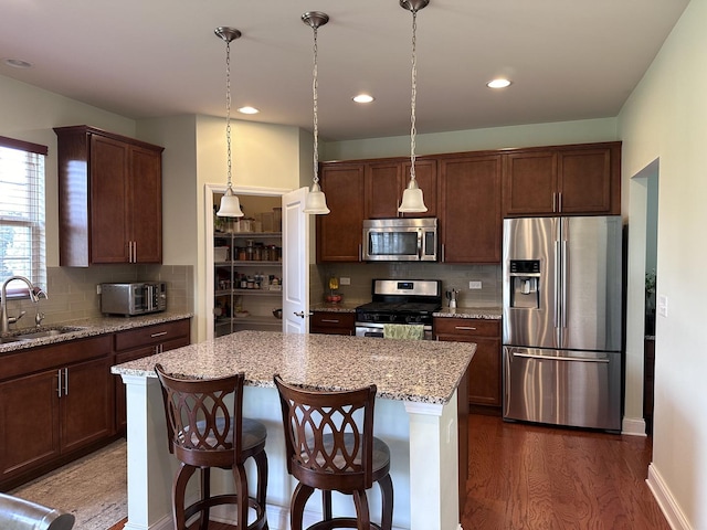 kitchen with sink, stainless steel appliances, a center island, light stone counters, and decorative light fixtures