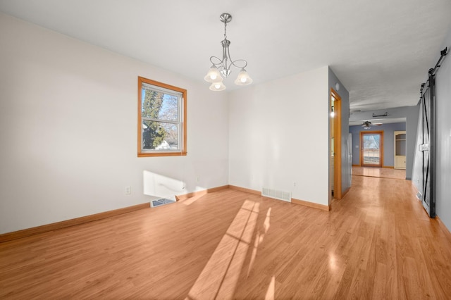 unfurnished room featuring a barn door, light wood-type flooring, and visible vents