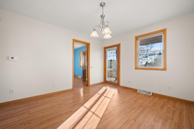 empty room featuring baseboards, visible vents, light wood finished floors, and an inviting chandelier