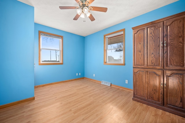 unfurnished bedroom with a textured ceiling, a ceiling fan, baseboards, visible vents, and light wood-style floors