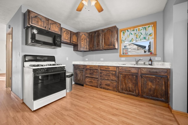 kitchen with light wood finished floors, black microwave, a sink, and gas stove