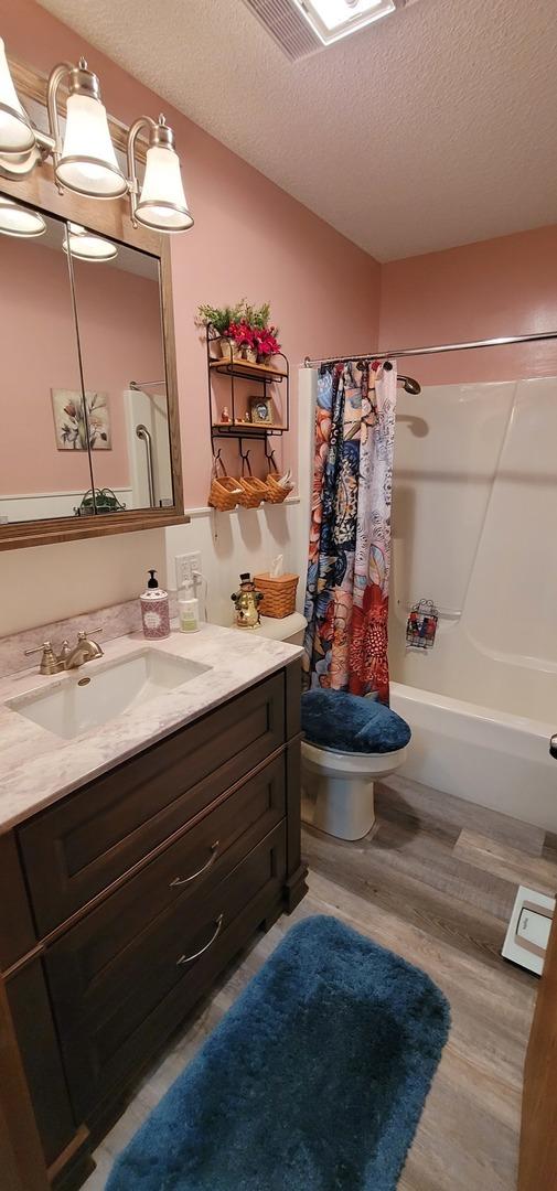 full bathroom featuring toilet, wood-type flooring, a textured ceiling, vanity, and shower / bath combo with shower curtain