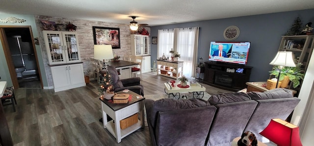 living room featuring dark wood-type flooring, ceiling fan, and a textured ceiling