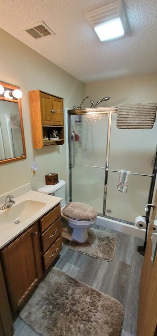 bathroom with a shower with door, hardwood / wood-style floors, vanity, a textured ceiling, and vaulted ceiling