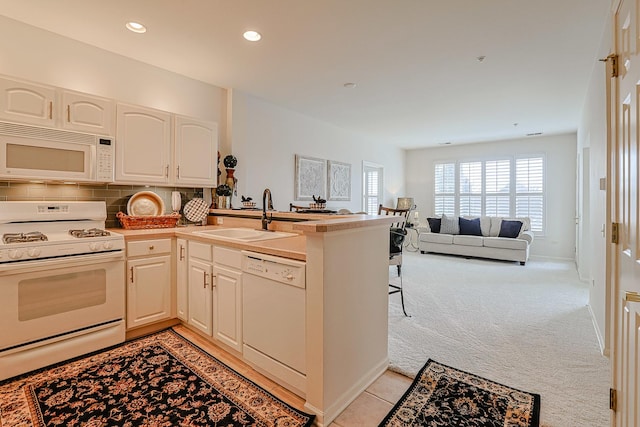 kitchen featuring sink, light carpet, white appliances, and kitchen peninsula