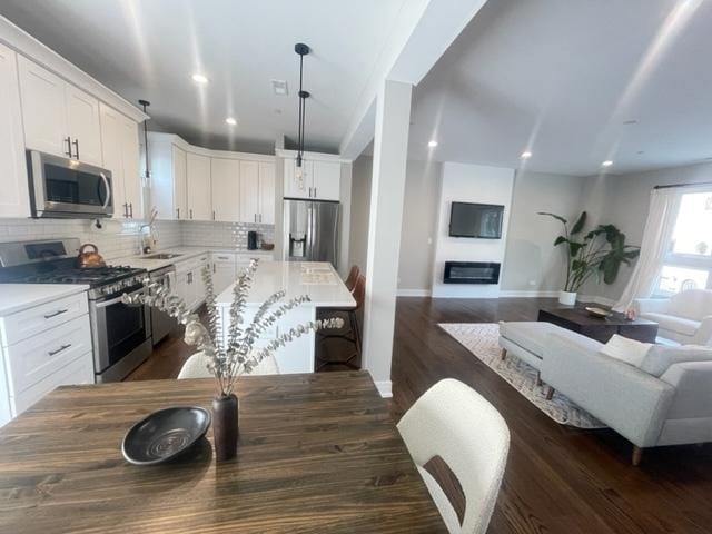 kitchen with pendant lighting, white cabinetry, backsplash, dark hardwood / wood-style flooring, and stainless steel appliances