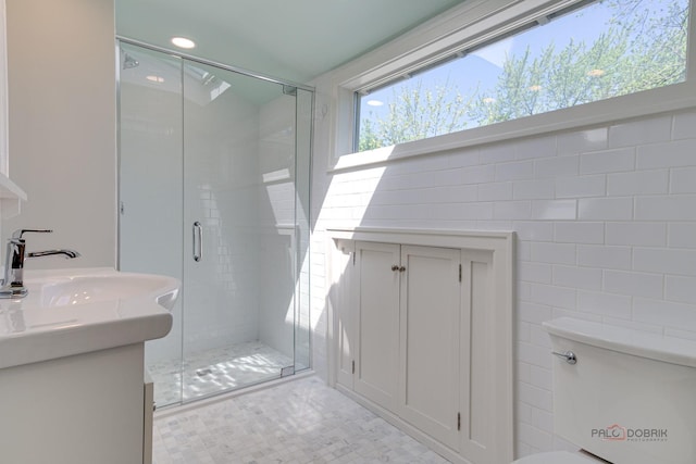 bathroom with a shower with door, vanity, tile walls, and toilet