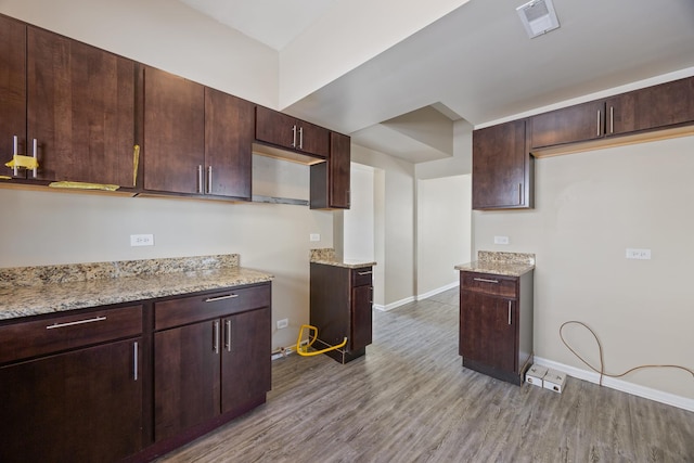 kitchen with dark brown cabinetry, light stone countertops, and light hardwood / wood-style flooring