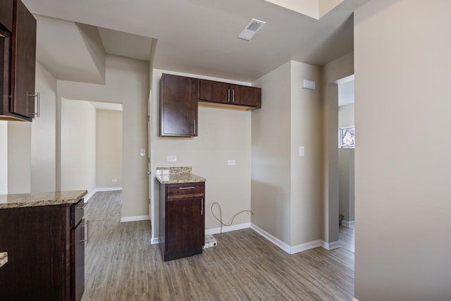 kitchen featuring dark brown cabinetry, light stone counters, and light hardwood / wood-style flooring