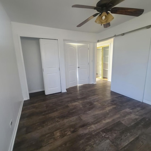 unfurnished bedroom with dark hardwood / wood-style floors, ceiling fan, and a barn door