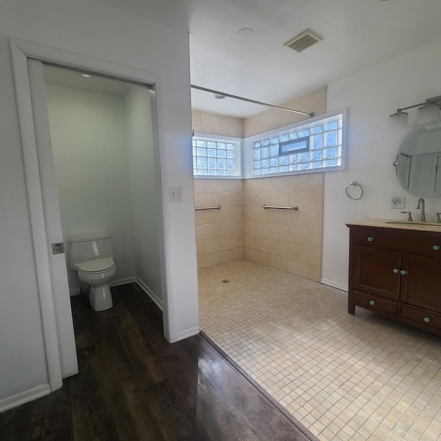 bathroom featuring hardwood / wood-style flooring, tiled shower, vanity, and toilet