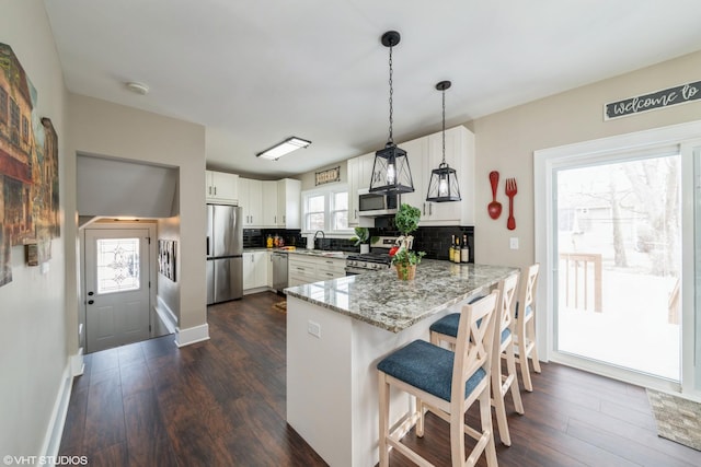 kitchen featuring appliances with stainless steel finishes, white cabinetry, a kitchen bar, decorative light fixtures, and kitchen peninsula