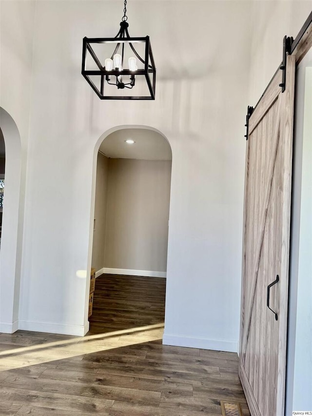 corridor with a barn door, dark wood-type flooring, and an inviting chandelier