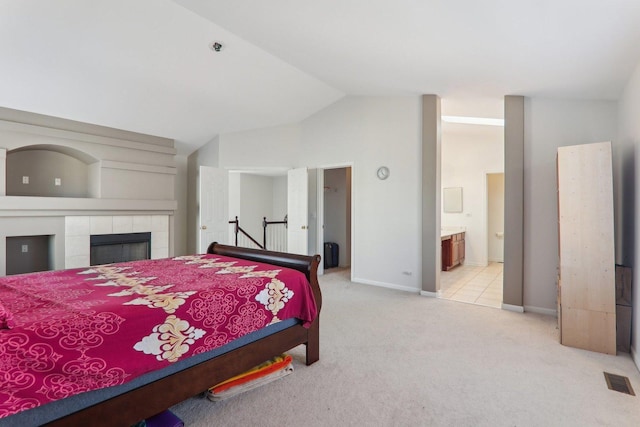 bedroom featuring lofted ceiling, ensuite bathroom, a fireplace, and light colored carpet