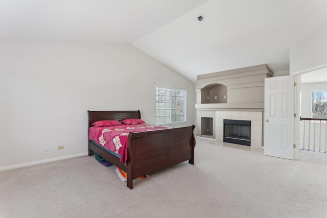 bedroom with multiple windows, a tiled fireplace, lofted ceiling, and light colored carpet