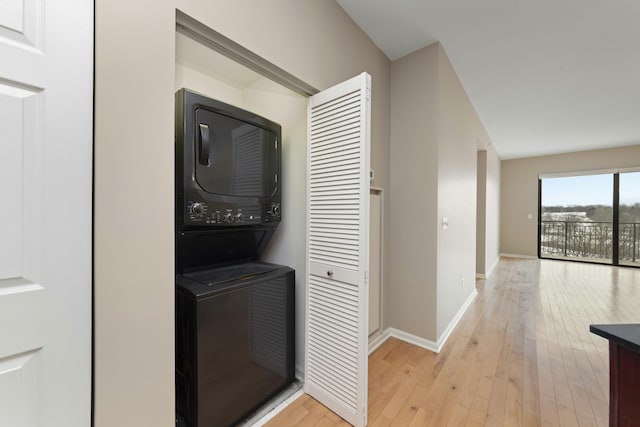 laundry area with stacked washer and clothes dryer and light wood-type flooring