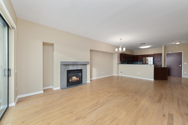 unfurnished living room featuring light hardwood / wood-style floors, a tile fireplace, and a chandelier