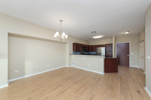 kitchen featuring a chandelier, hanging light fixtures, stainless steel fridge, kitchen peninsula, and light hardwood / wood-style floors