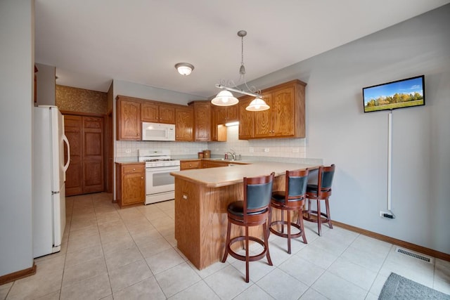 kitchen with sink, a breakfast bar area, hanging light fixtures, kitchen peninsula, and white appliances