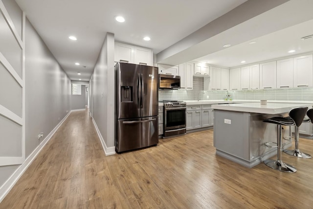 kitchen with appliances with stainless steel finishes, a breakfast bar, white cabinets, backsplash, and light wood-type flooring