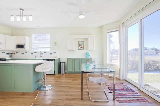 kitchen featuring dishwasher, a kitchen breakfast bar, stainless steel microwave, green cabinetry, and decorative light fixtures