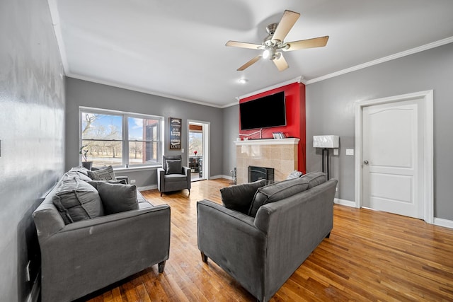 living room featuring a tiled fireplace, crown molding, ceiling fan, and light wood-type flooring