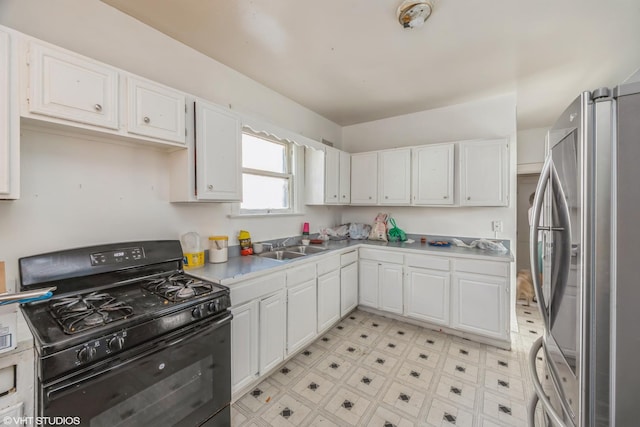 kitchen with black gas stove, sink, white cabinets, and stainless steel refrigerator