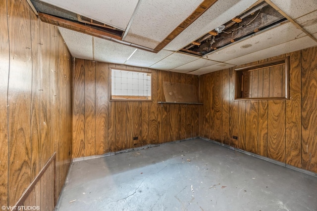 basement featuring a drop ceiling and wood walls