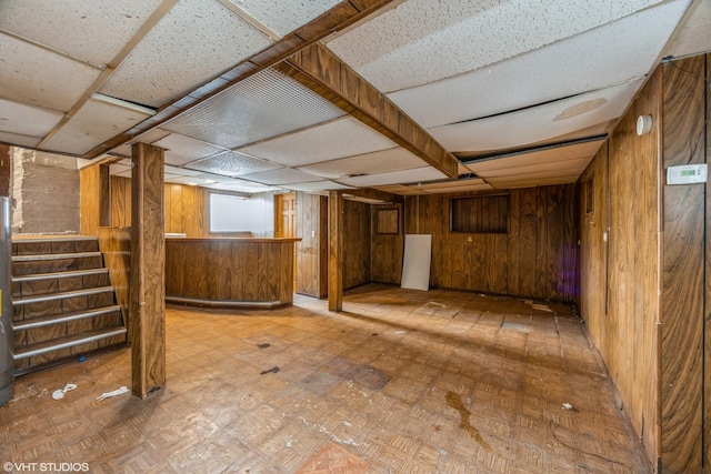 basement featuring a drop ceiling and wooden walls