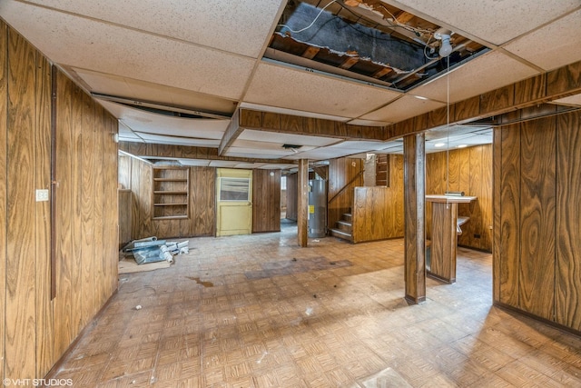 basement featuring wood walls, a drop ceiling, light parquet floors, and gas water heater