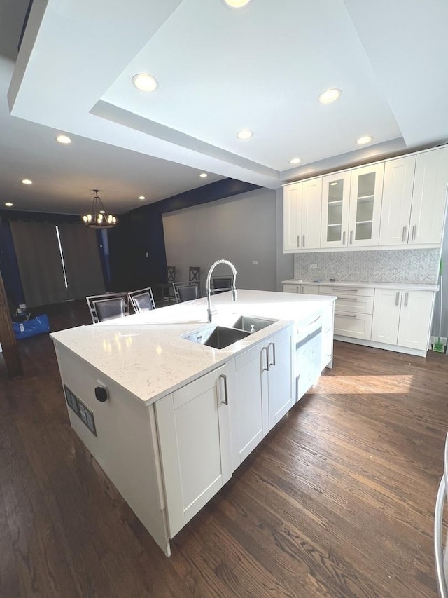 kitchen featuring white cabinetry, an island with sink, sink, backsplash, and light stone counters