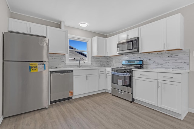 kitchen featuring appliances with stainless steel finishes, tasteful backsplash, white cabinetry, sink, and light wood-type flooring