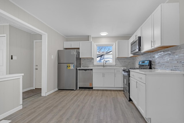 kitchen with tasteful backsplash, white cabinetry, sink, light hardwood / wood-style floors, and stainless steel appliances