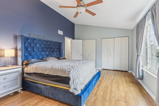 bedroom with ceiling fan, lofted ceiling, light hardwood / wood-style floors, and two closets