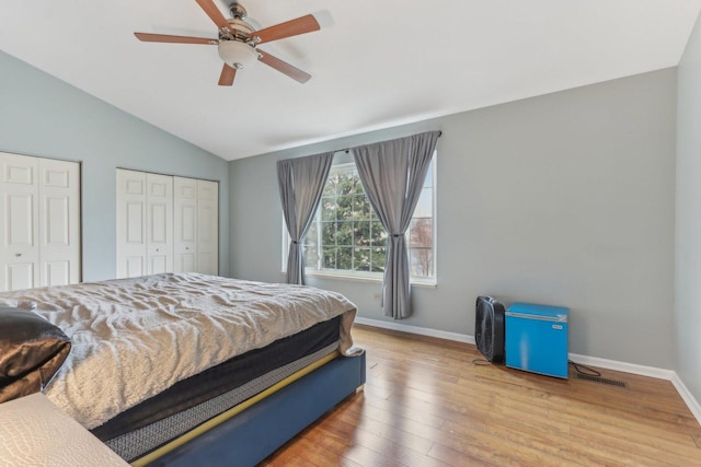 bedroom featuring two closets, vaulted ceiling, ceiling fan, and light wood-type flooring