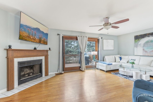 living room with a tiled fireplace, light hardwood / wood-style floors, and ceiling fan