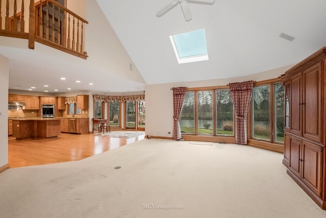 unfurnished living room featuring high vaulted ceiling, light colored carpet, ceiling fan, and a skylight