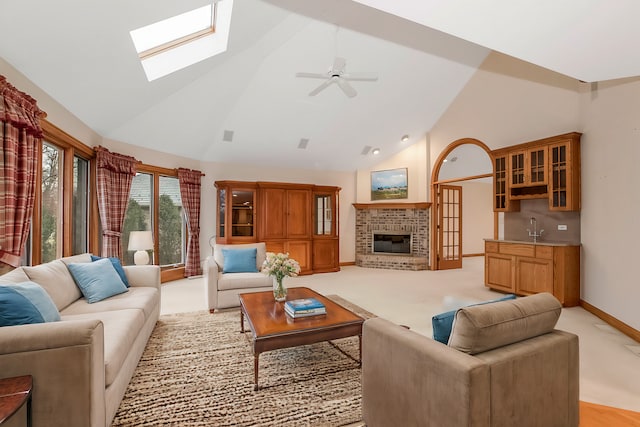 carpeted living room with sink, a skylight, high vaulted ceiling, ceiling fan, and a fireplace