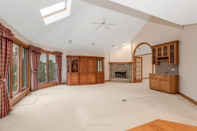 living room with sink, light colored carpet, high vaulted ceiling, a brick fireplace, and ceiling fan