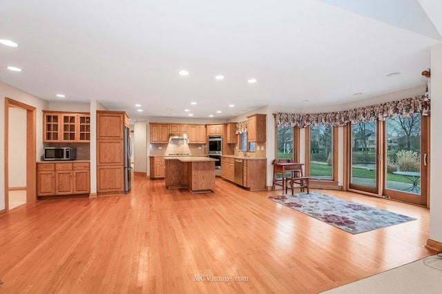 kitchen with stainless steel appliances, a center island, ventilation hood, and light wood-type flooring