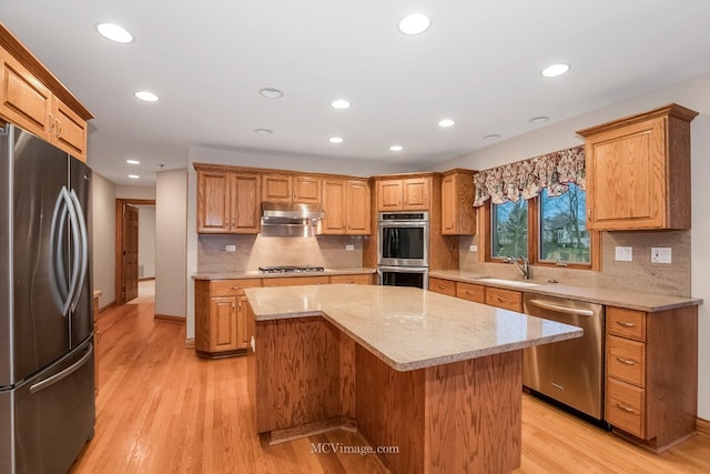 kitchen featuring a kitchen island, sink, light stone counters, light hardwood / wood-style floors, and stainless steel appliances