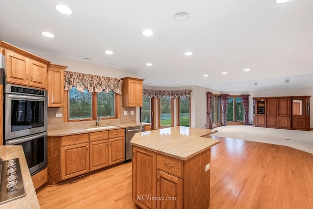 kitchen featuring a kitchen island, appliances with stainless steel finishes, sink, decorative backsplash, and light wood-type flooring