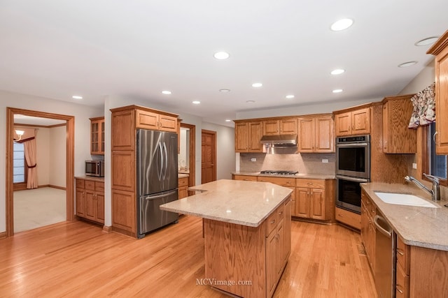 kitchen featuring sink, appliances with stainless steel finishes, backsplash, light stone countertops, and a kitchen island