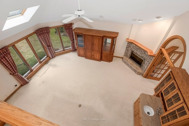 living room featuring ceiling fan, a brick fireplace, vaulted ceiling with skylight, and light carpet