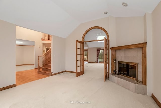 unfurnished living room with a tiled fireplace, lofted ceiling, carpet floors, and french doors