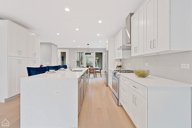 kitchen featuring white cabinetry, decorative light fixtures, stainless steel gas range, and an island with sink