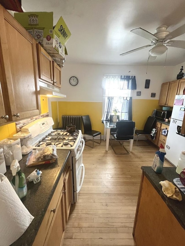 kitchen with radiator heating unit, dark stone counters, ceiling fan, white gas range oven, and light wood-type flooring