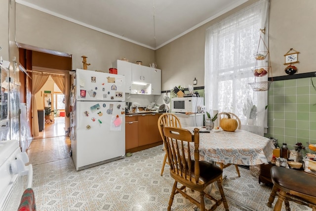 kitchen with white appliances, ornamental molding, and white cabinets